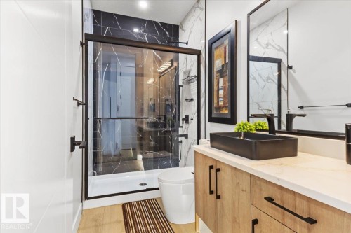 Contemporary bathroom featuring a glass-enclosed shower with black-veined wall tile, a black rectangular vessel sink, and a wood-finish vanity with dark hardware - 6903 169 Avenue Nw, Edmonton, AB - Indoor