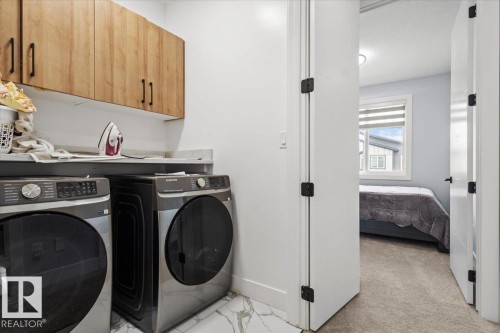 Laundry area with wood-finish upper cabinetry, a light-toned countertop, and integrated appliances - 6903 169 Avenue Nw, Edmonton, AB - Indoor Photo Showing Laundry Room