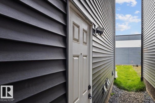 Dark gray horizontal siding with a white panel door and an exterior light fixture - 6903 169 Avenue Nw, Edmonton, AB - Outdoor With Exterior
