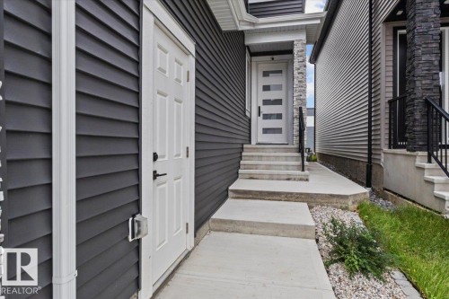 Modern entry door with frosted glass panels, stone column accents, concrete steps with metal railings, and dark horizontal siding - 6903 169 Avenue Nw, Edmonton, AB - Outdoor