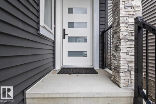 Modern entry door with frosted glass panels, dark horizontal siding, stone pillar accent, and black metal railing - 6903 169 Avenue Nw, Edmonton, AB - Outdoor With Exterior
