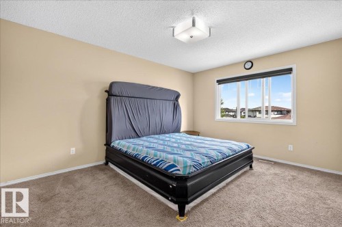 Neutral tone wall paint, textured ceiling, carpeted flooring, and a large window with blinds - 1529 26 Ave Nw Nw, Edmonton, AB - Indoor Photo Showing Bedroom