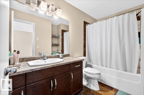 Bathroom featuring a dark wood-finish vanity with a light-toned countertop, a rectangular undermount sink, and a multi-bulb vanity light fixture - 1529 26 Ave Nw Nw, Edmonton, AB - Indoor Photo Showing Bathroom