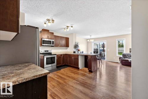 Open-concept kitchen featuring wood-finish flooring, stainless steel appliances, dark wood cabinetry, an island with seating, and a sliding glass door - 1529 26 Ave Nw Nw, Edmonton, AB - Indoor Photo Showing Kitchen