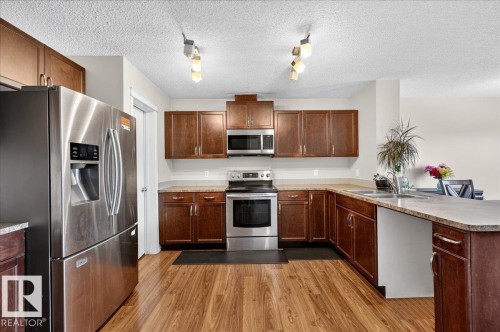 Kitchen featuring wood-finish flooring, stainless steel appliances, dark wood cabinetry, and light-toned countertops - 1529 26 Ave Nw Nw, Edmonton, AB - Indoor Photo Showing Kitchen With Double Sink
