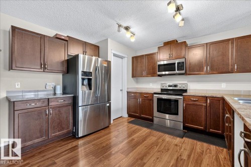 Wood-finish flooring, dark wood cabinetry, stainless steel appliances, and track lighting fixtures - 1529 26 Ave Nw Nw, Edmonton, AB - Indoor Photo Showing Kitchen