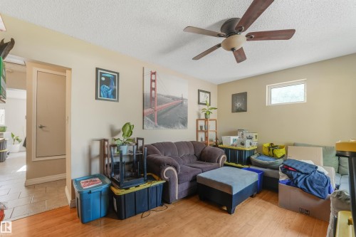 Spacious living room featuring warm wood-finish flooring, ceiling fan with brushed metal blades, and neutral wall finishes - 12209 94 Street Nw, Edmonton, AB - Indoor