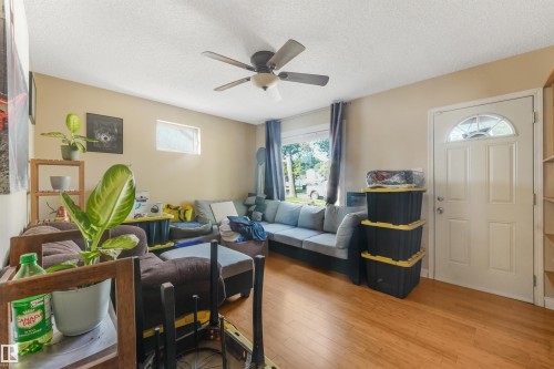 Wood-finish flooring, ceiling fan with integrated lighting, natural light from the large front window, and an arched transom entry door - 12209 94 Street Nw, Edmonton, AB - Indoor Photo Showing Other Room