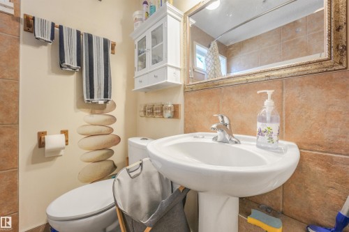 Pedestal sink with chrome faucet, complemented by a rectangular framed mirror and wall-mounted storage cabinet - 12209 94 Street Nw, Edmonton, AB - Indoor Photo Showing Bathroom