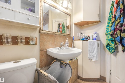 Pedestal sink with chrome faucet, wall-mounted mirror, overhead vanity lighting, white toilet, and built-in white cabinetry - 12209 94 Street Nw, Edmonton, AB - Indoor Photo Showing Bathroom