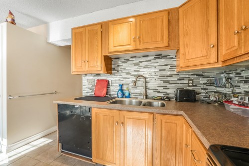 Kitchen featuring wood cabinetry, stainless steel double basin sink, modern tile backsplash, and durable countertops - 12209 94 Street Nw, Edmonton, AB - Indoor Photo Showing Kitchen With Double Sink