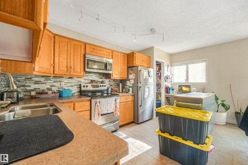Kitchen featuring wood cabinetry, stainless steel appliances, a multi-tone tile backsplash, and a double basin sink - 12209 94 Street Nw, Edmonton, AB - Indoor Photo Showing Kitchen With Double Sink