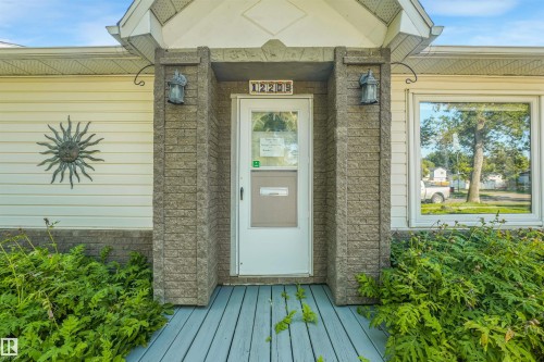 Front entry featuring a light blue wood-finish porch, stone-finish columns, and exterior lighting fixtures - 12209 94 Street Nw, Edmonton, AB - Outdoor With Exterior