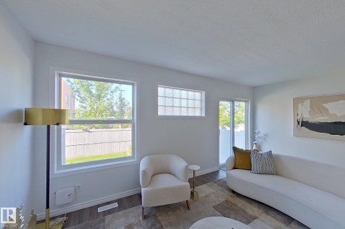 Bright living space with wood-finish flooring, white walls, large window, glass block window, and a sliding glass door - #7 16823 84 St Nw Nw, Edmonton, AB - Indoor Photo Showing Living Room