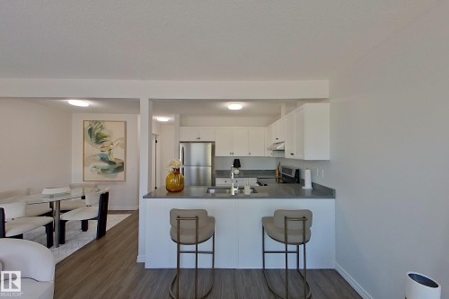 Kitchen featuring white cabinetry, stainless steel refrigerator, grey countertops, and wood-finish flooring - #7 16823 84 St Nw Nw, Edmonton, AB - Indoor Photo Showing Kitchen