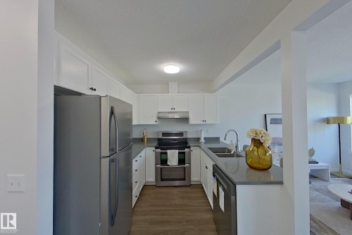 U-shaped kitchen featuring wood-finish flooring, white cabinetry, dark countertops, and stainless steel appliances - #7 16823 84 St Nw Nw, Edmonton, AB - Indoor Photo Showing Kitchen With Double Sink