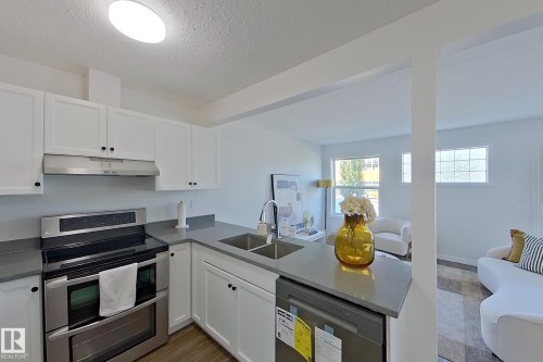 Kitchen featuring white shaker cabinetry, stainless steel appliances, a double basin sink, and wood-finish flooring - #7 16823 84 St Nw Nw, Edmonton, AB - Indoor Photo Showing Kitchen With Double Sink