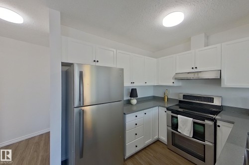Contemporary kitchen featuring white cabinetry, stainless steel appliances, dark countertops, and wood-finish flooring - #7 16823 84 St Nw Nw, Edmonton, AB - Indoor Photo Showing Kitchen