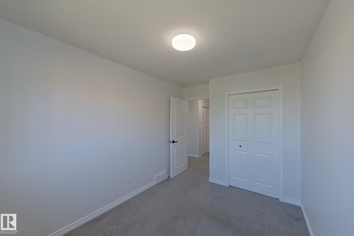 Neutral wall paint, light gray carpeting, white bi-fold closet doors, white interior door with black hardware, and a flush-mount ceiling light - #7 16823 84 St Nw Nw, Edmonton, AB - Indoor Photo Showing Other Room