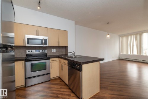 Kitchen featuring stainless steel appliances, dark countertops, and light wood-finish cabinetry - #1004 10136 104 St Nw, Edmonton, AB - Indoor Photo Showing Kitchen With Stainless Steel Kitchen With Double Sink