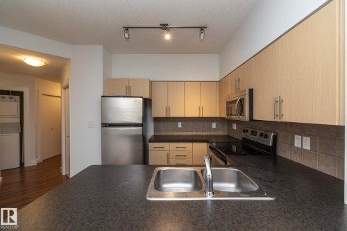 Kitchen featuring wood-finish cabinetry, stainless steel appliances, black countertops, and a double basin sink - #1004 10136 104 St Nw, Edmonton, AB - Indoor Photo Showing Kitchen With Stainless Steel Kitchen With Double Sink