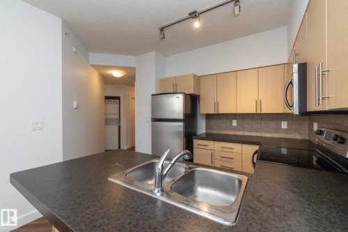 Kitchen featuring stainless steel appliances, wood-finish cabinetry, a dual basin sink, and track lighting - #1004 10136 104 St Nw, Edmonton, AB - Indoor Photo Showing Kitchen With Double Sink