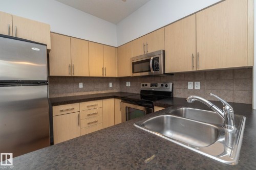 Kitchen featuring stainless steel appliances, light wood-finish cabinetry, dark countertops, and a double basin sink with a chrome faucet - #1004 10136 104 St Nw, Edmonton, AB - Indoor Photo Showing Kitchen With Stainless Steel Kitchen With Double Sink