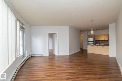 Expansive living area featuring wood-finish flooring, a curved window line, and white vertical blinds - #1004 10136 104 St Nw, Edmonton, AB - Indoor