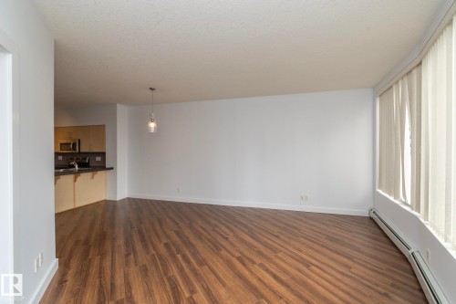 Wood-finish flooring throughout, white walls, and a recessed kitchen with light wood-tone cabinetry - #1004 10136 104 St Nw, Edmonton, AB - Indoor