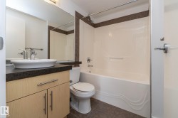 Full vanity mirror, vessel sink, wood-finish cabinetry, dark countertop, and a tiled tub surround - 