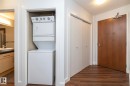 Integrated stacked washer and dryer in a dedicated closet, complemented by wood-finish flooring, a solid core wood entry door, and white bi-fold closet doors - #1004 10136 104 St Nw, Edmonton, AB  - Indoor Photo Showing Laundry Room 