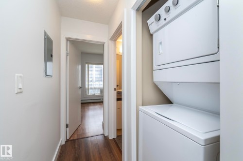 Hallway featuring wood-finish flooring, white walls, and a stacked washer and dryer - #1004 10136 104 St Nw, Edmonton, AB - Indoor Photo Showing Laundry Room