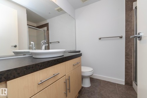 Modern vanity with a vessel sink, dark countertop, and light wood-finish cabinetry - #1004 10136 104 St Nw, Edmonton, AB - Indoor Photo Showing Bathroom
