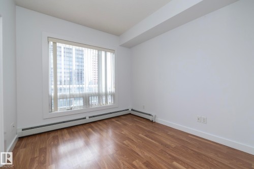 Expansive window with roller blinds, wood-finish flooring, white walls, and baseboard heating - #1004 10136 104 St Nw, Edmonton, AB - Indoor Photo Showing Other Room