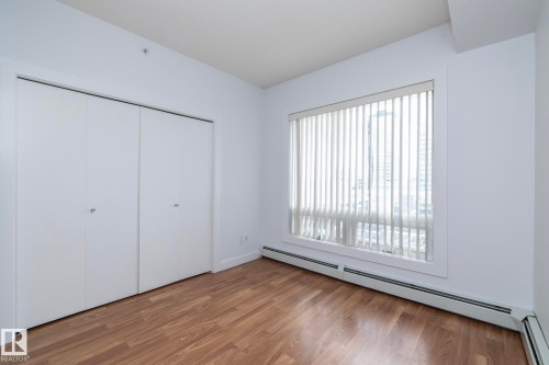 Wood-finish flooring, white bi-fold closet doors, and large window with vertical blinds - #1004 10136 104 St Nw, Edmonton, AB - Indoor Photo Showing Other Room