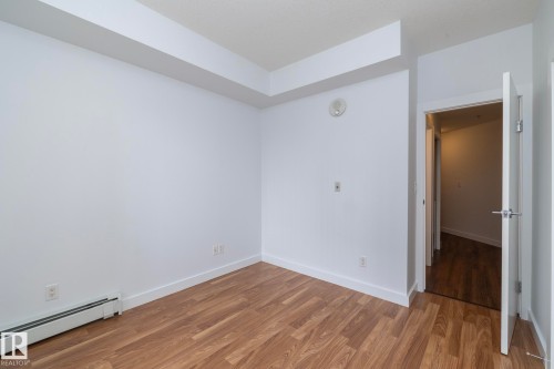 Wood-finish flooring with white baseboards, white walls, and a white interior door with a brushed nickel lever - #1004 10136 104 St Nw, Edmonton, AB - Indoor Photo Showing Other Room