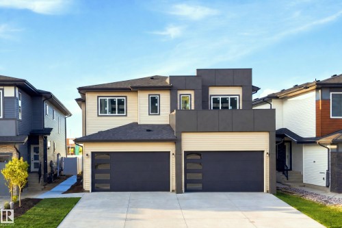 Modern exterior featuring a two-story design, dual garage doors with frosted glass panels, light-colored siding, and dark accent paneling - 1818 155 Avenue Nw, Edmonton, AB - Outdoor With Facade