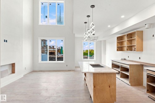 Open-concept area featuring high ceilings, light wood-finish flooring, and a kitchen island with an integrated sink - 1818 155 Avenue Nw, Edmonton, AB - Indoor