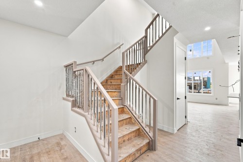 Light wood-finish flooring, staircase with painted wood railings and metal balusters, white paneled door with matte black hardware, recessed ceiling lighting, and large windows - 1818 155 Avenue Nw, Edmonton, AB - Indoor Photo Showing Other Room