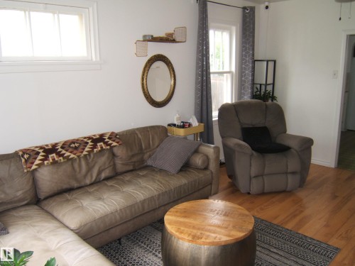 Living area featuring wood-finish flooring, white painted walls, and multiple windows with natural light - 5530 50 Street, Vegreville, AB 