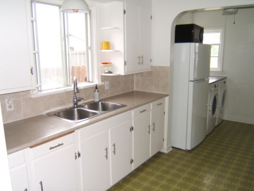 Kitchen featuring white cabinetry, a double basin stainless steel sink with a high-arc faucet, and tiled backsplash - 5530 50 Street, Vegreville, AB 