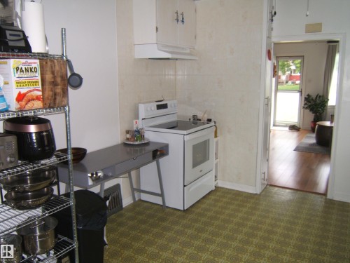 Kitchen featuring patterned vinyl flooring, white appliances, and a built-in range hood - 5530 50 Street, Vegreville, AB 