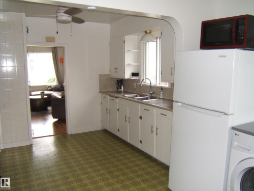 Kitchen featuring patterned flooring, white cabinetry, and a double basin sink - 5530 50 Street, Vegreville, AB 