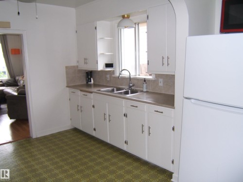 Kitchen featuring white cabinetry, a double basin sink, neutral countertops, and a ceramic tile backsplash - 5530 50 Street, Vegreville, AB 