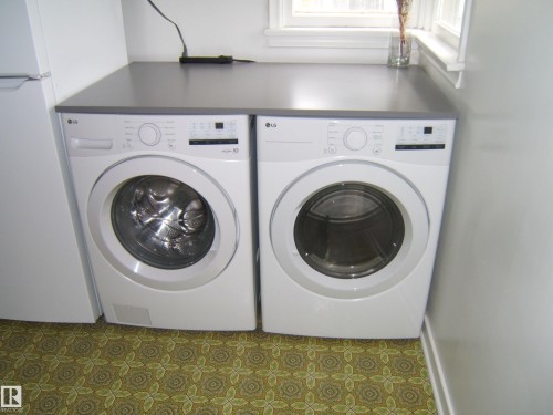 Laundry area featuring front-loading washer and dryer units, a dark countertop, and decorative patterned flooring - 5530 50 Street, Vegreville, AB 