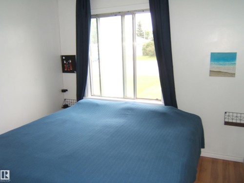 Hardwood-finish flooring and white walls complement the large window with dark curtains - 5530 50 Street, Vegreville, AB 