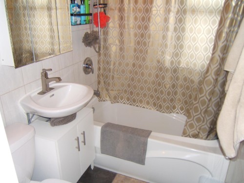 Bathroom featuring white tiled walls, a white ceramic sink with a brushed nickel faucet, and a white vanity cabinet with brushed nickel hardware - 5530 50 Street, Vegreville, AB 