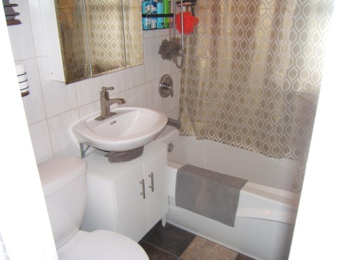 Bathroom featuring white ceramic wall tiling, a white vanity with a basin sink, a wall-mounted mirrored cabinet, a white toilet, and a white bathtub - 5530 50 Street, Vegreville, AB 