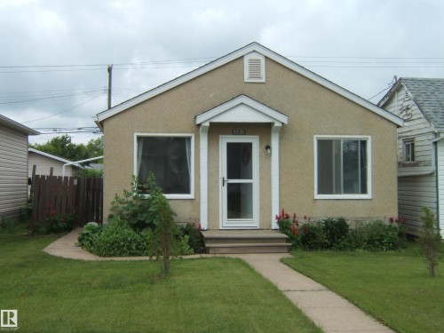 Stucco exterior featuring white trim and a gabled roofline - 5530 50 Street, Vegreville, AB 