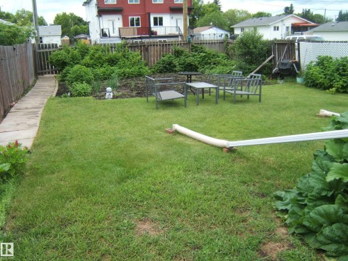 Spacious backyard featuring a large grass lawn, perimeter fencing, mature shrubbery, and a paved walkway - 5530 50 Street, Vegreville, AB 